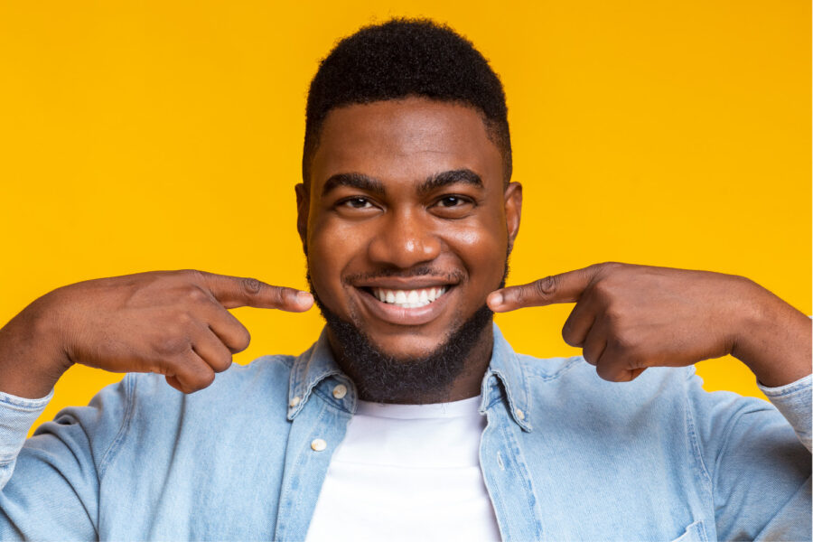 Dark-haired man smiles and points to his white teeth after professional teeth whitening