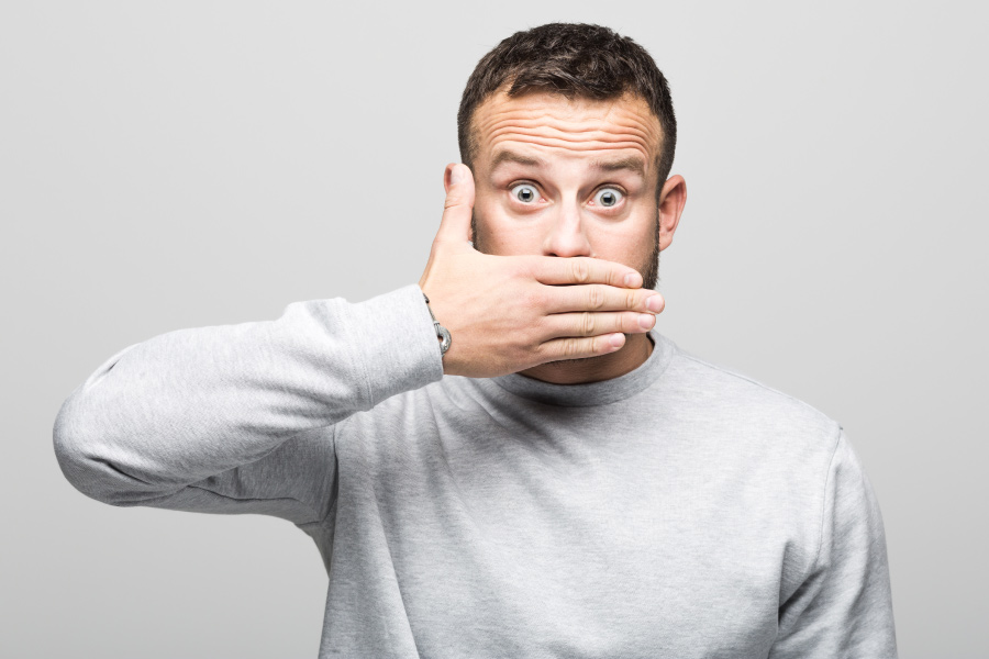 Brunette man in a gray shirt covers his mouth with his hand due to bad breath in Lowell, MA